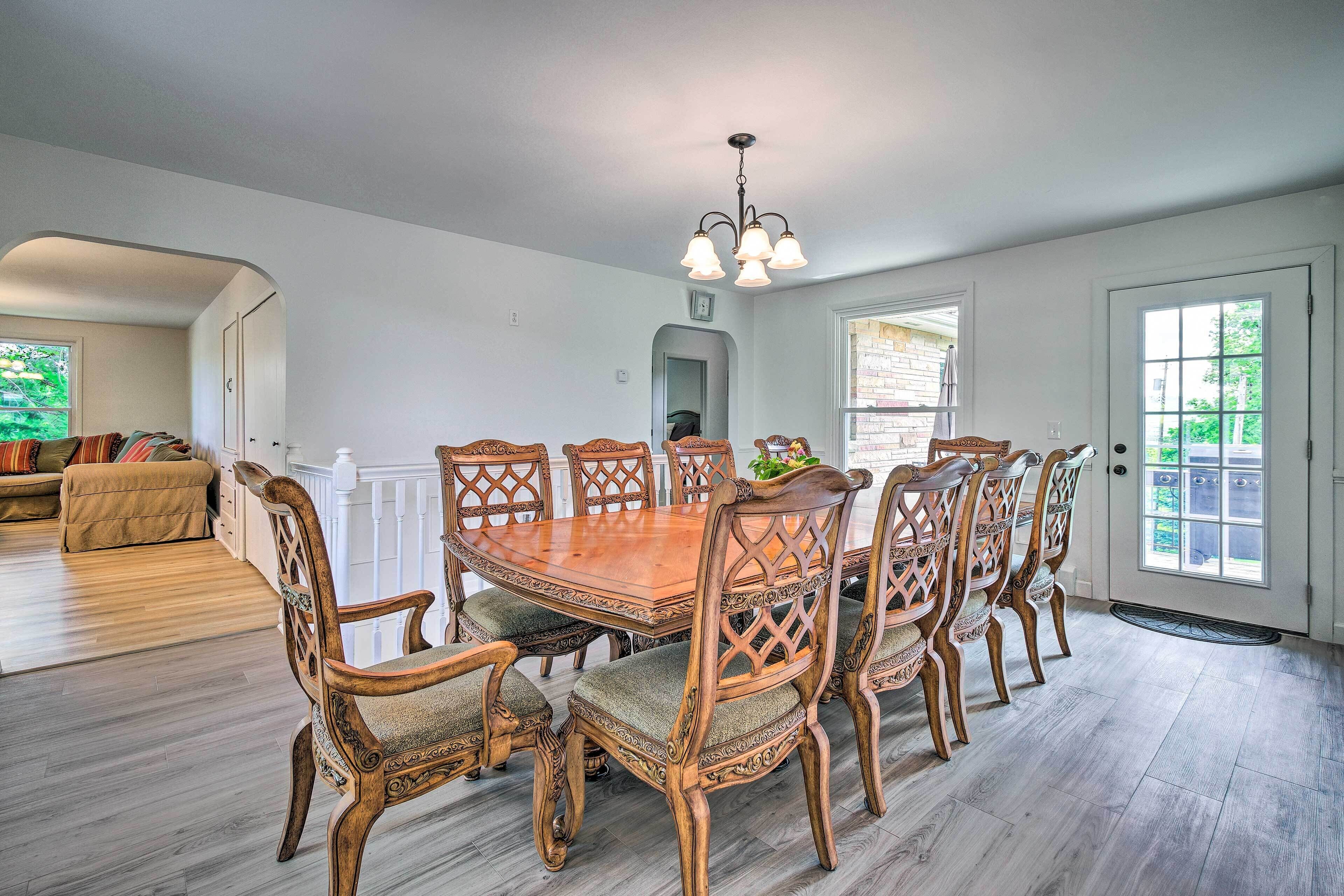 Une salle à manger avec une table et des chaises en bois, un lustre et une vue sur l’extérieur par une porte.