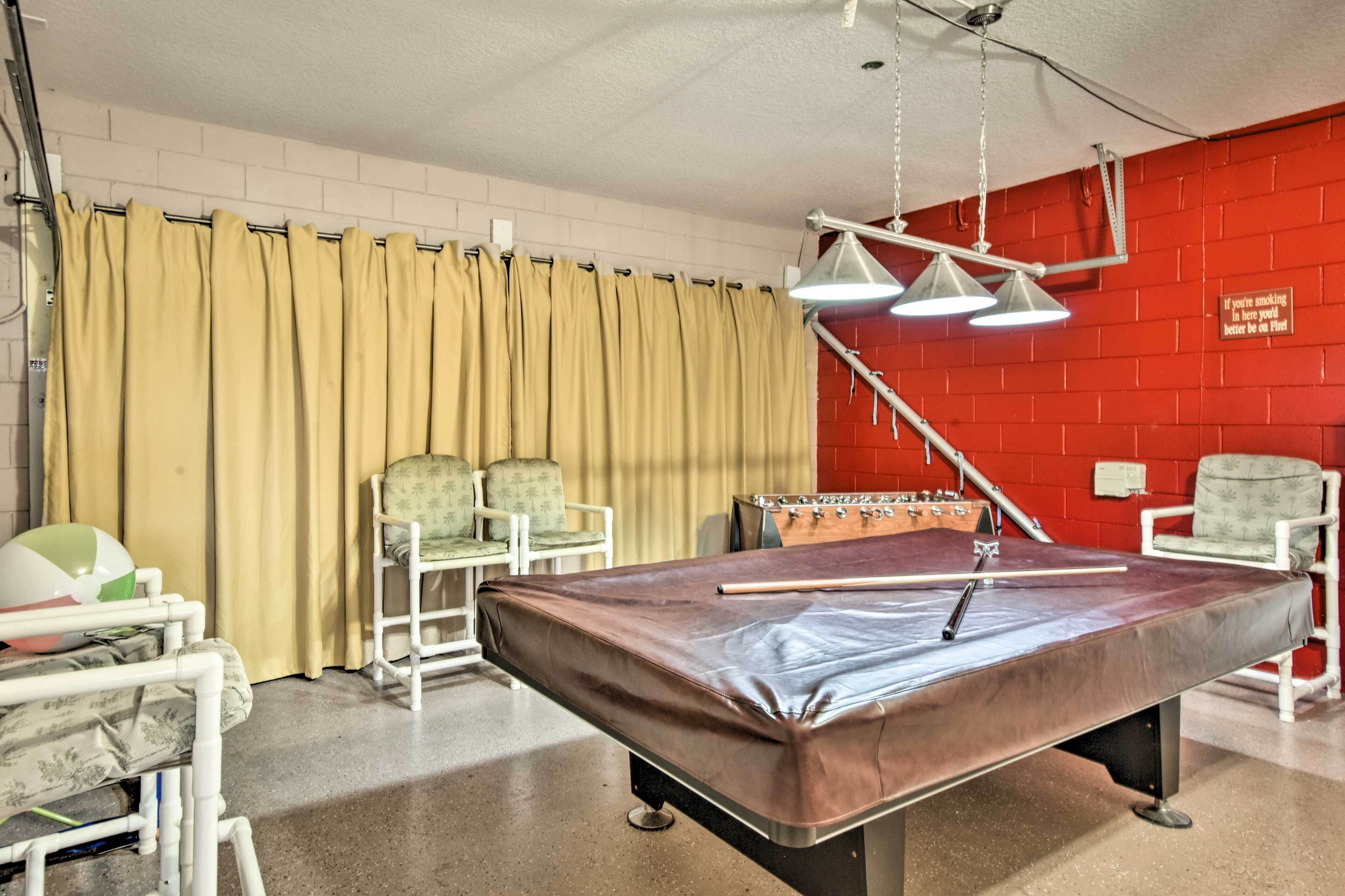 A pool table in a room with red brick walls, two chairs, and a foosball table.