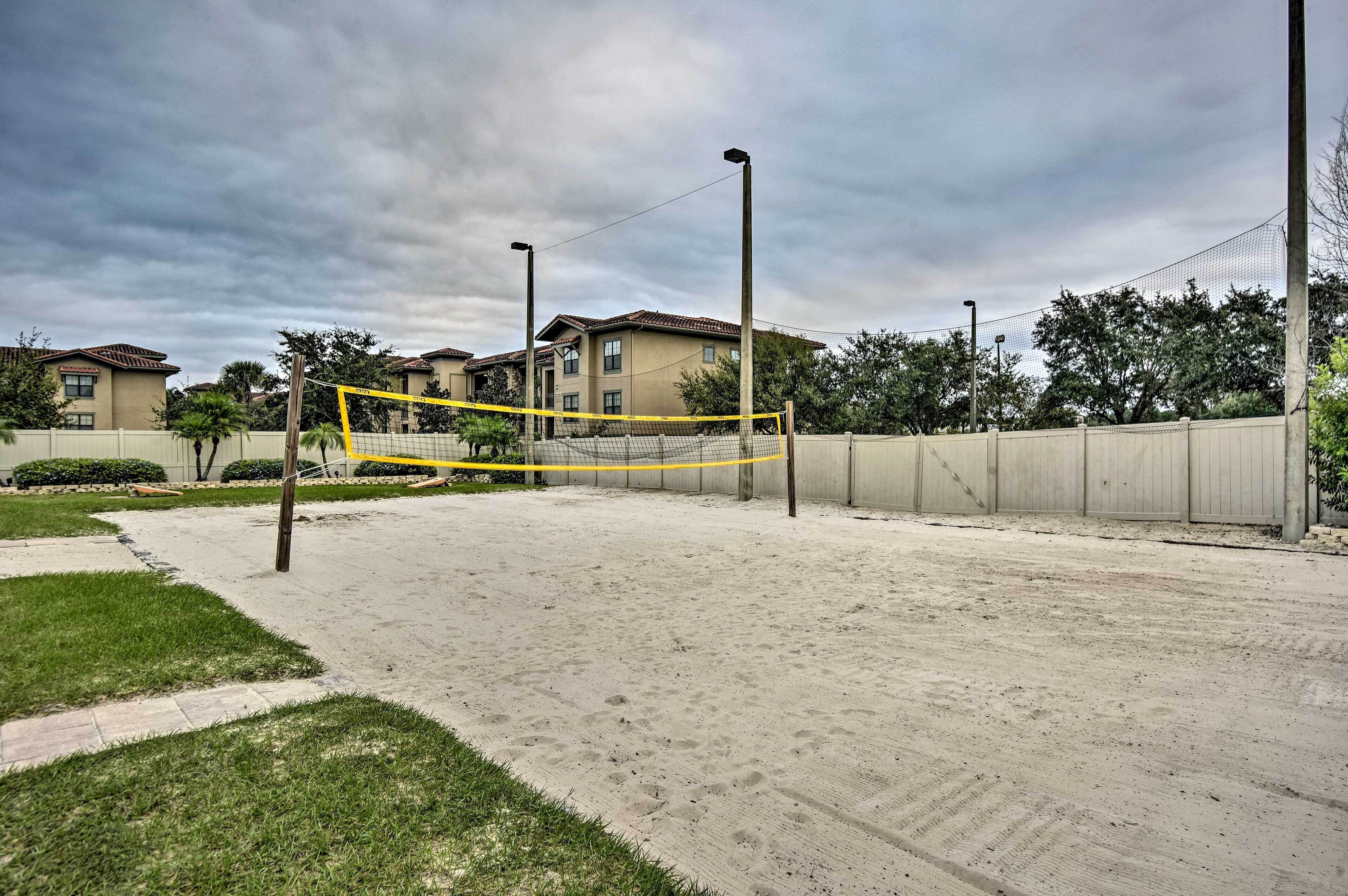 Un terrain de volley-ball avec un filet, entouré d’une zone sablonneuse et d’une petite clôture.