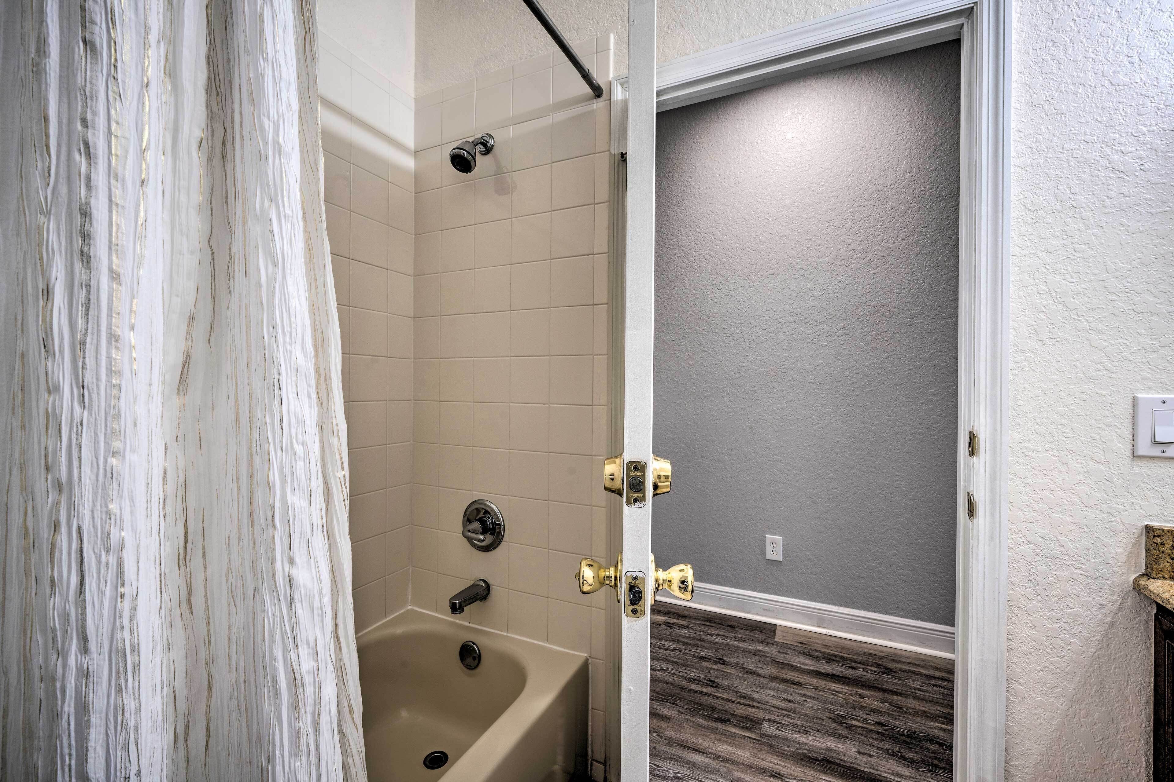 A bathroom with a bathtub, shower, and a door leading to another room.