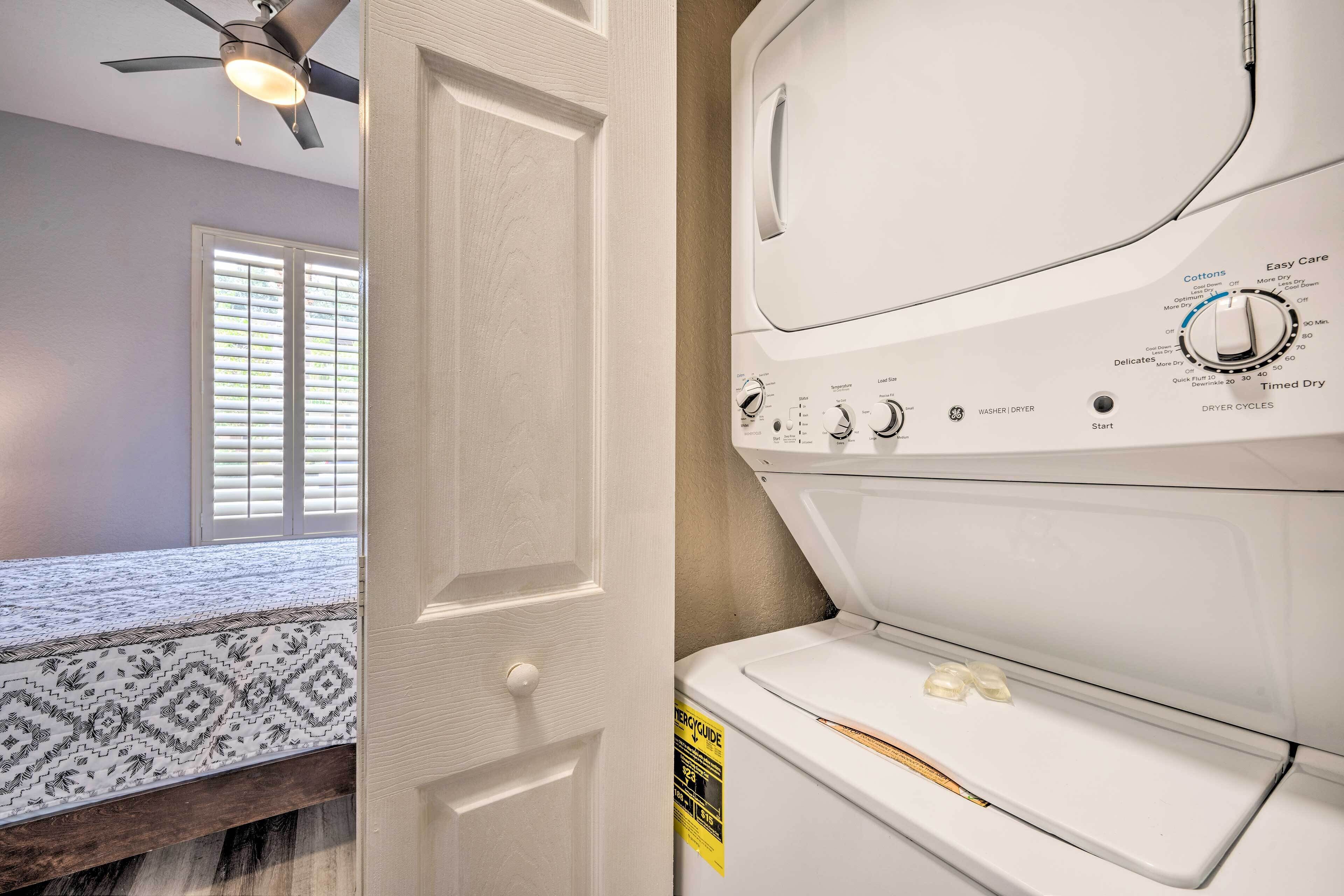 A laundry room with a front-loading washer and dryer, a ceiling fan, and a window with blinds.