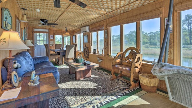 Interior acogedor de una cabaña con techo de madera, ventanas amplias, un sofá de cuero, una mesa de madera y vista a un lago.