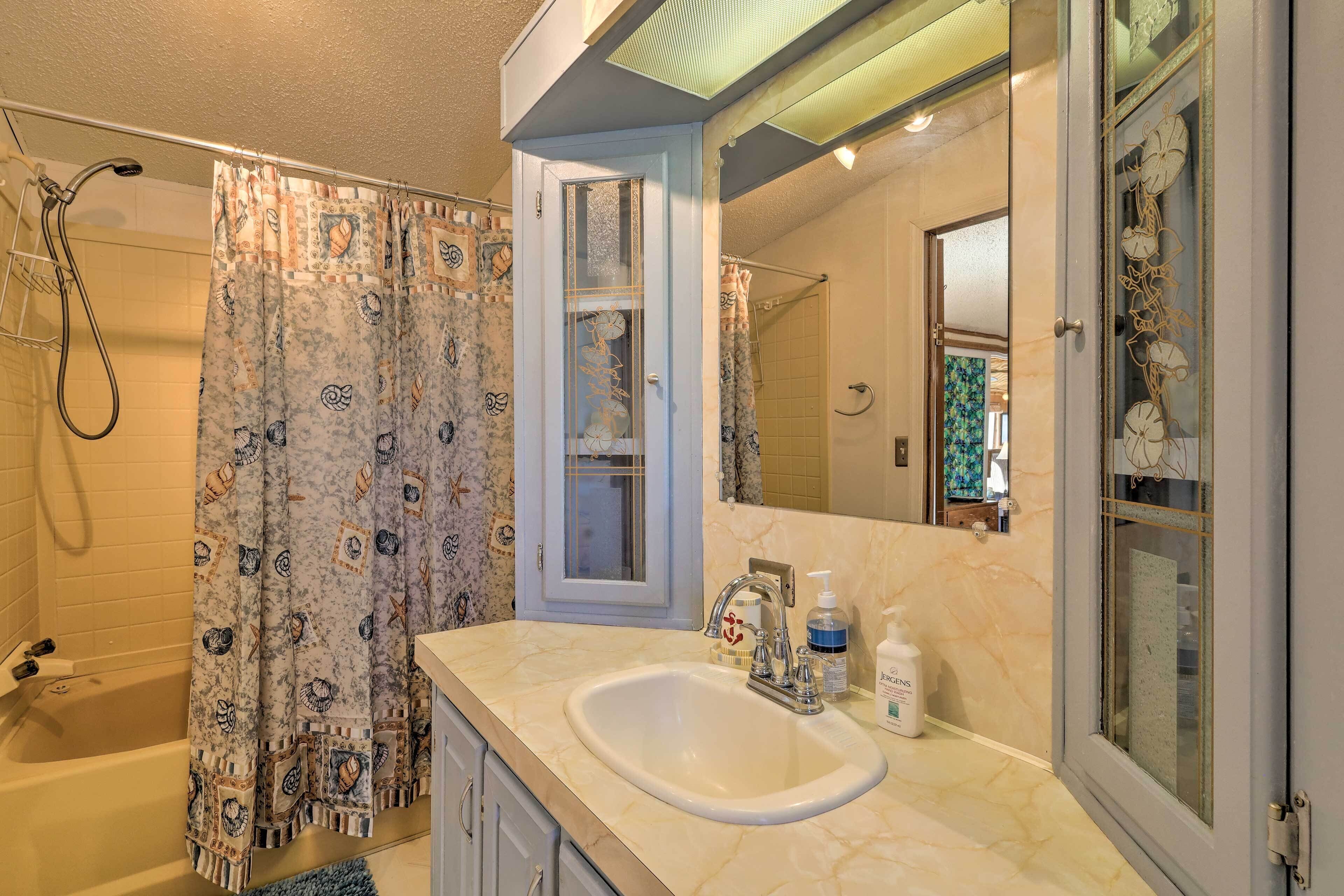 A bathroom with a bathtub, shower, and a sink with toiletries.