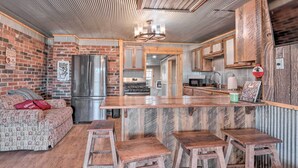 A rustic kitchen with a wooden bar, a refrigerator, and a sofa with patterned cushions. - Rustic Retreat - Steps to Pomme De Terre Lake (Flemington)