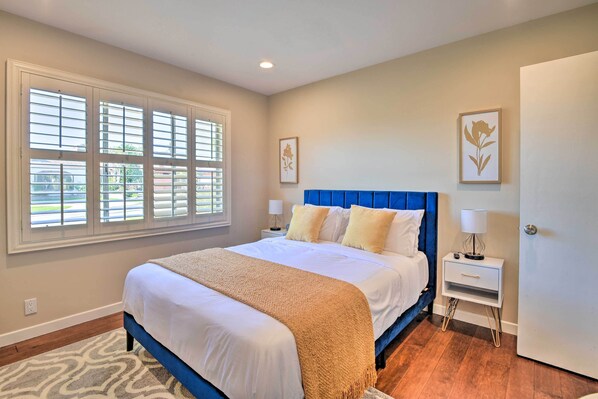 A bedroom with a bed, a nightstand, a window with blinds, and a door.