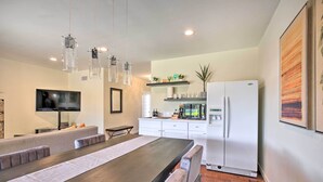 Una cocina moderna con una mesa larga de comedor, armarios blancos y un refrigerador.
