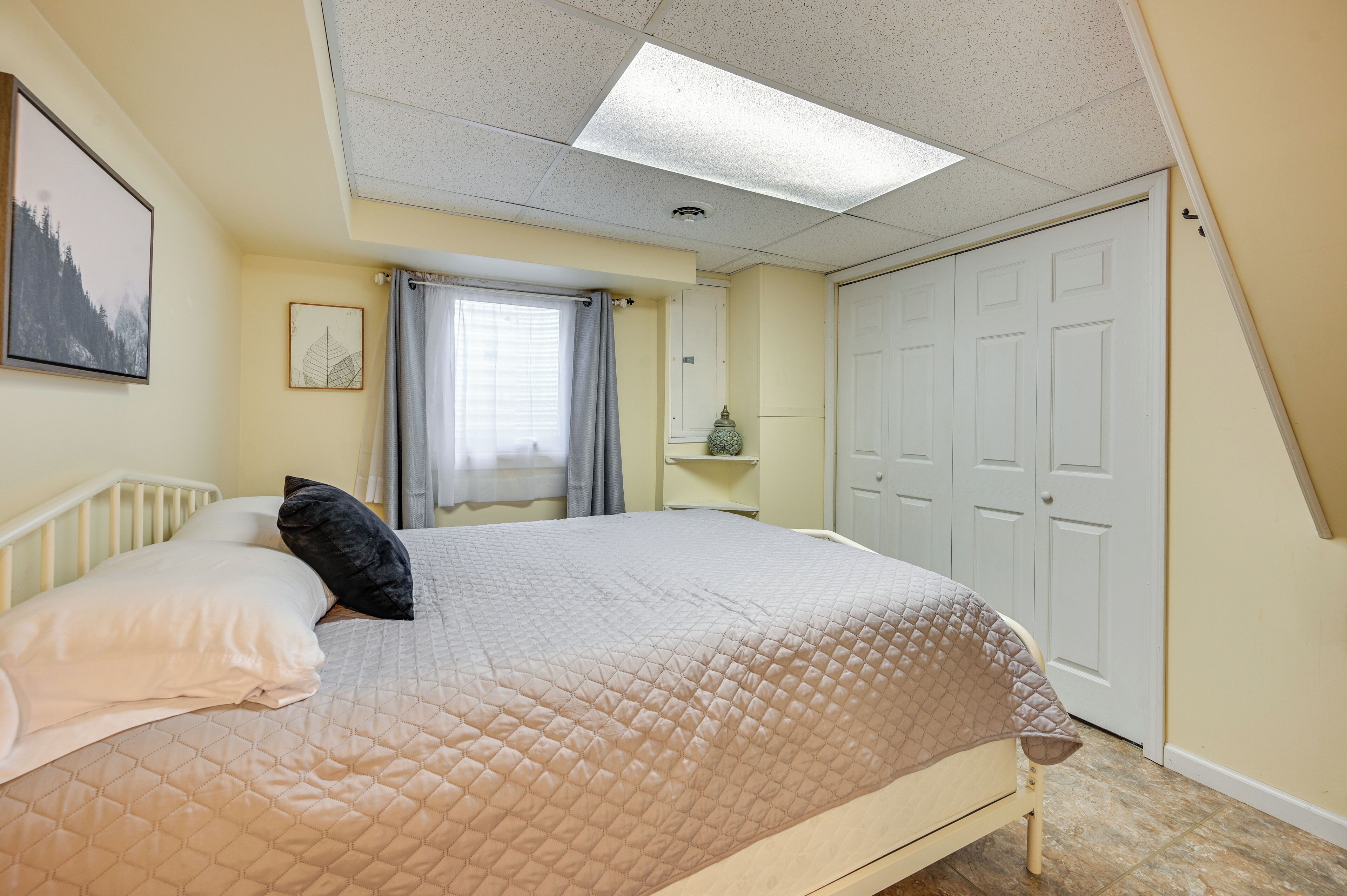Un dormitorio con cama, ventana con cortinas, una puerta y una lámpara en el techo.