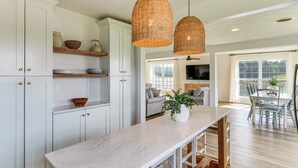 A kitchen with white cabinets, a marble countertop, wicker pendant lights, and a dining area with a table and chairs.