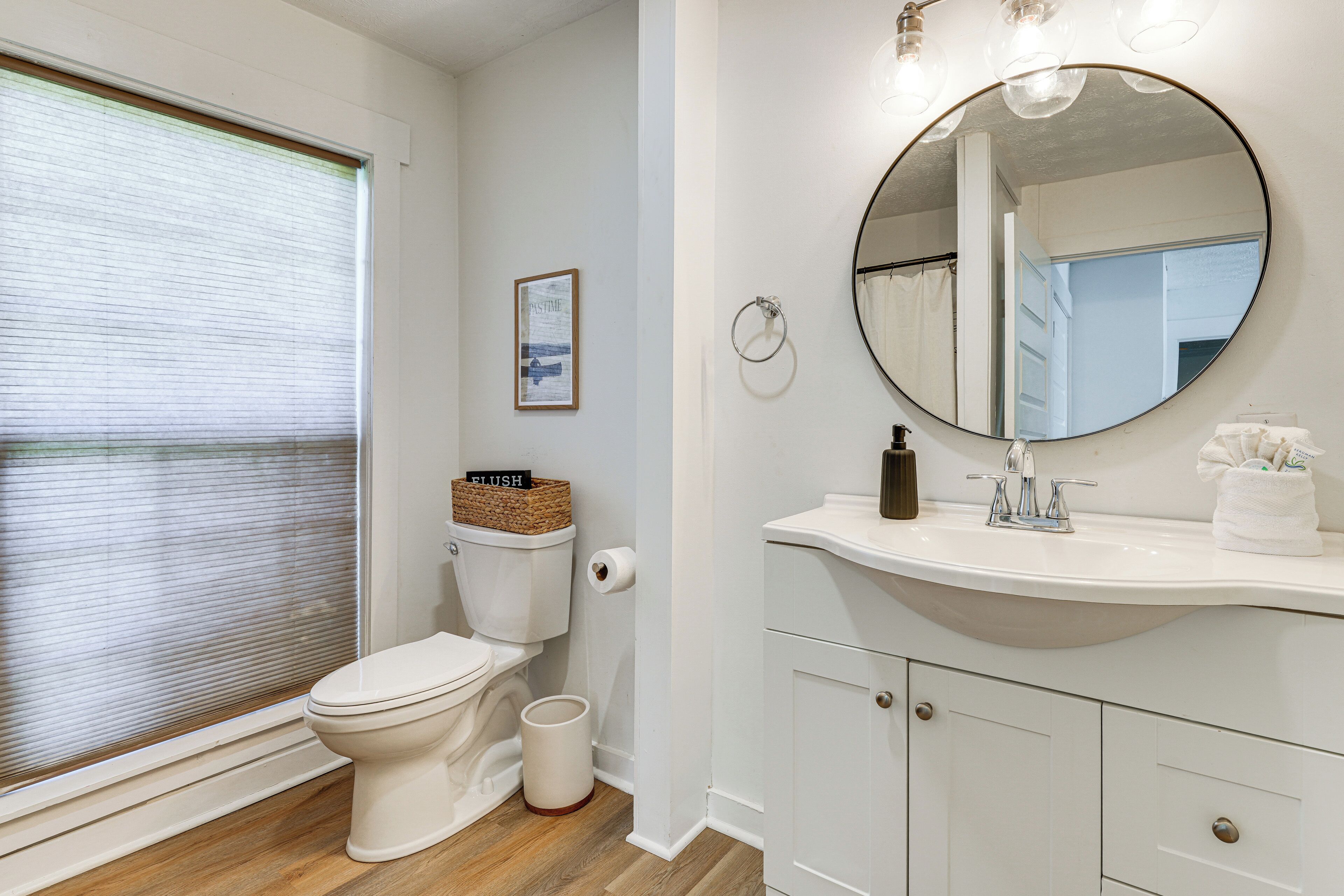 A bathroom with a toilet, sink, mirror, and a framed picture on the wall.