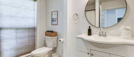 A bathroom with a toilet, sink, mirror, and a framed picture on the wall.
