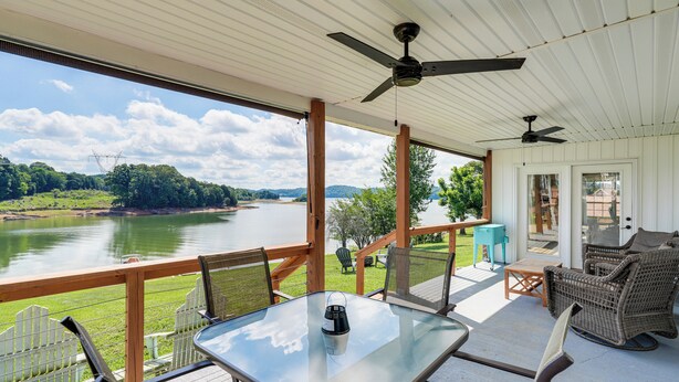 A covered outdoor deck with a table, chairs, and a view of a lake.