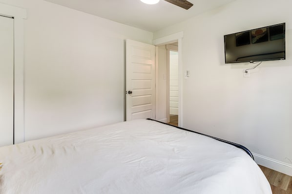Un dormitorio con una cama, una puerta y un televisor montado en la pared.