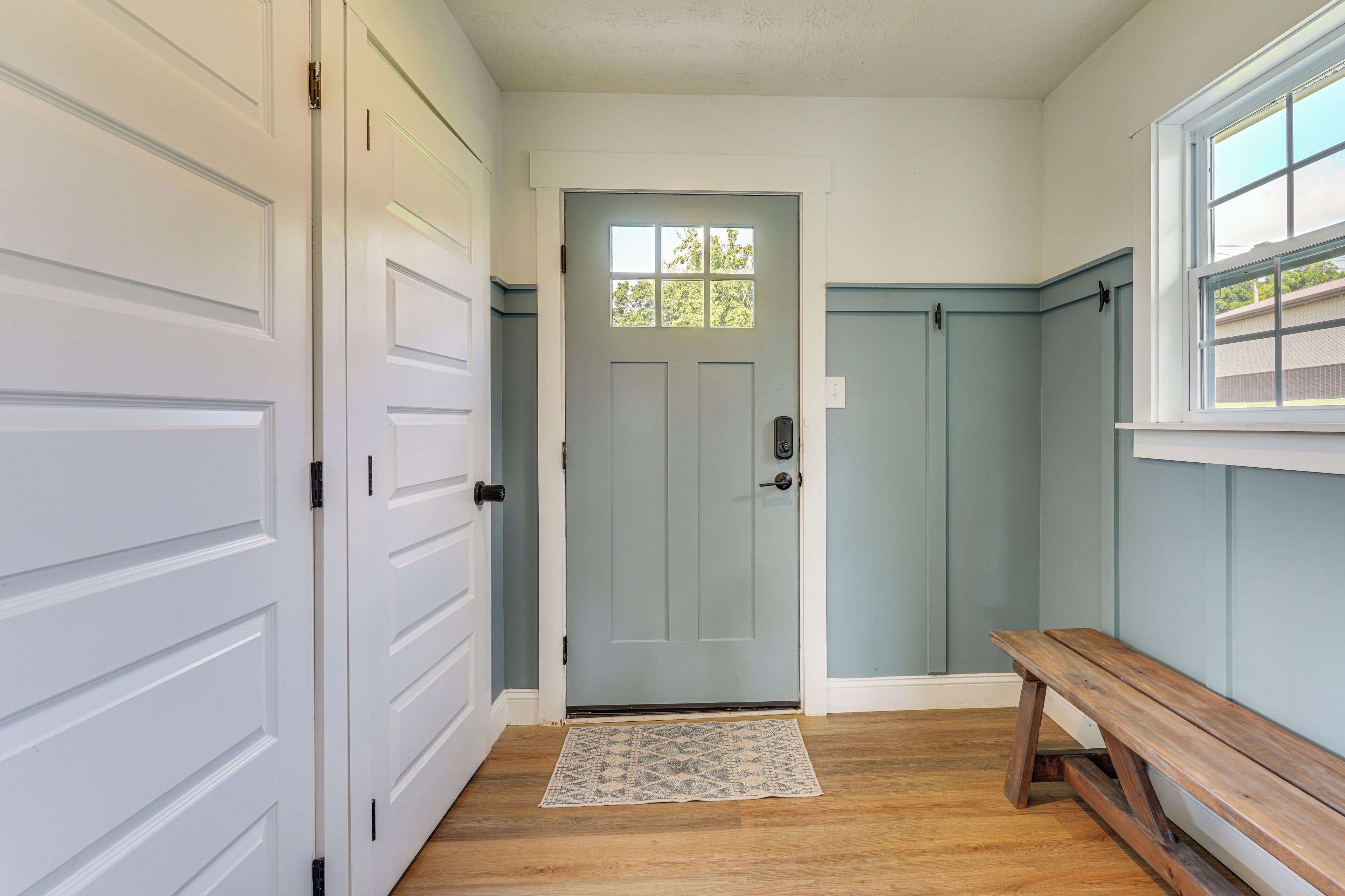 A hallway with a grey door, white doors, a wooden bench, and a patterned rug.