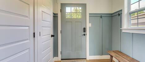 A hallway with a grey door, white doors, a wooden bench, and a patterned rug.