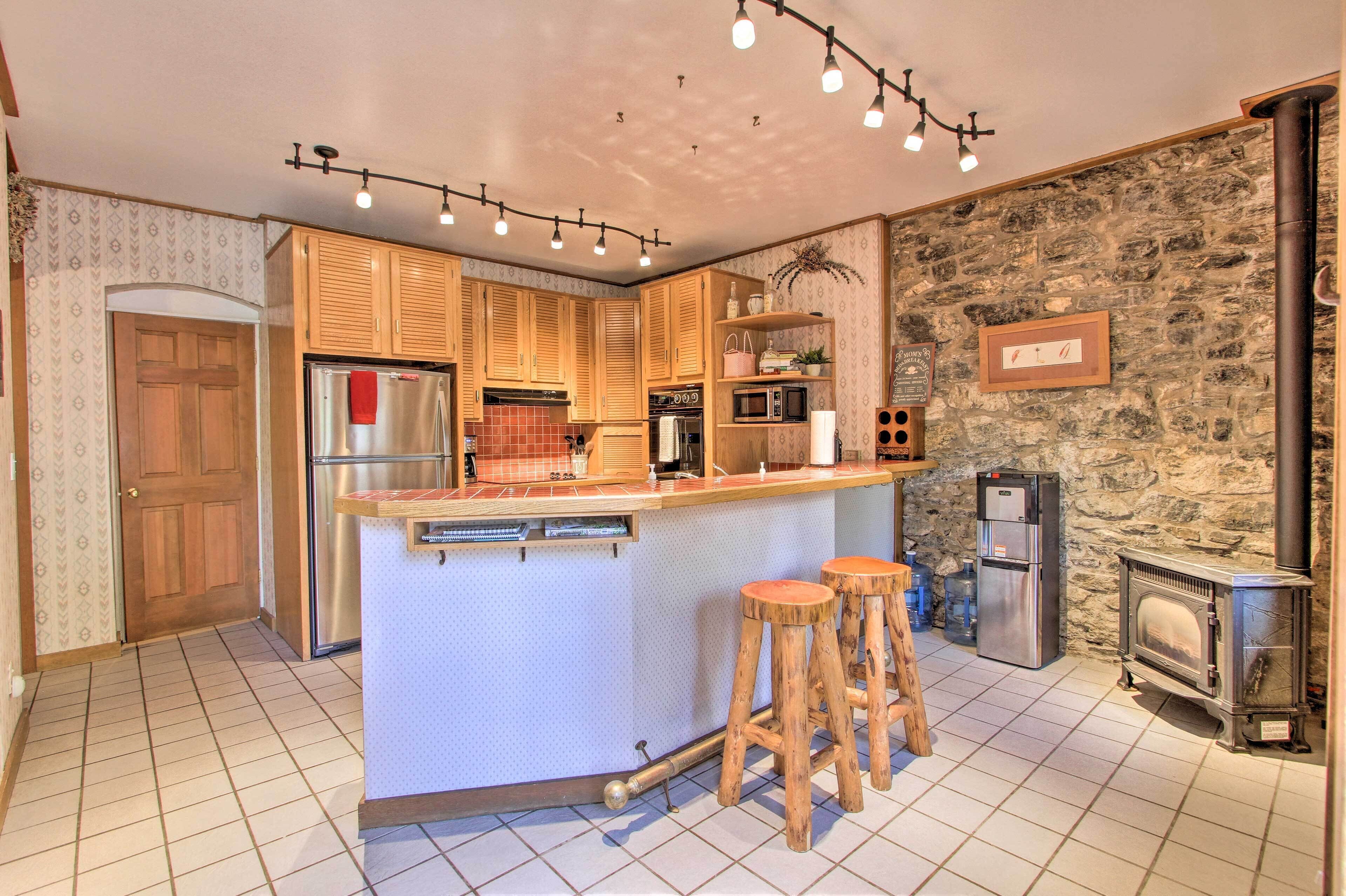 Una cocina con armarios de madera, una isla central con taburetes, una pared de piedra y un estufa de leña.