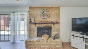 Ein Wohnzimmer mit Kamin aus Backstein, einem Fernseher und einer Schiebetür zu einem Außenbereich.