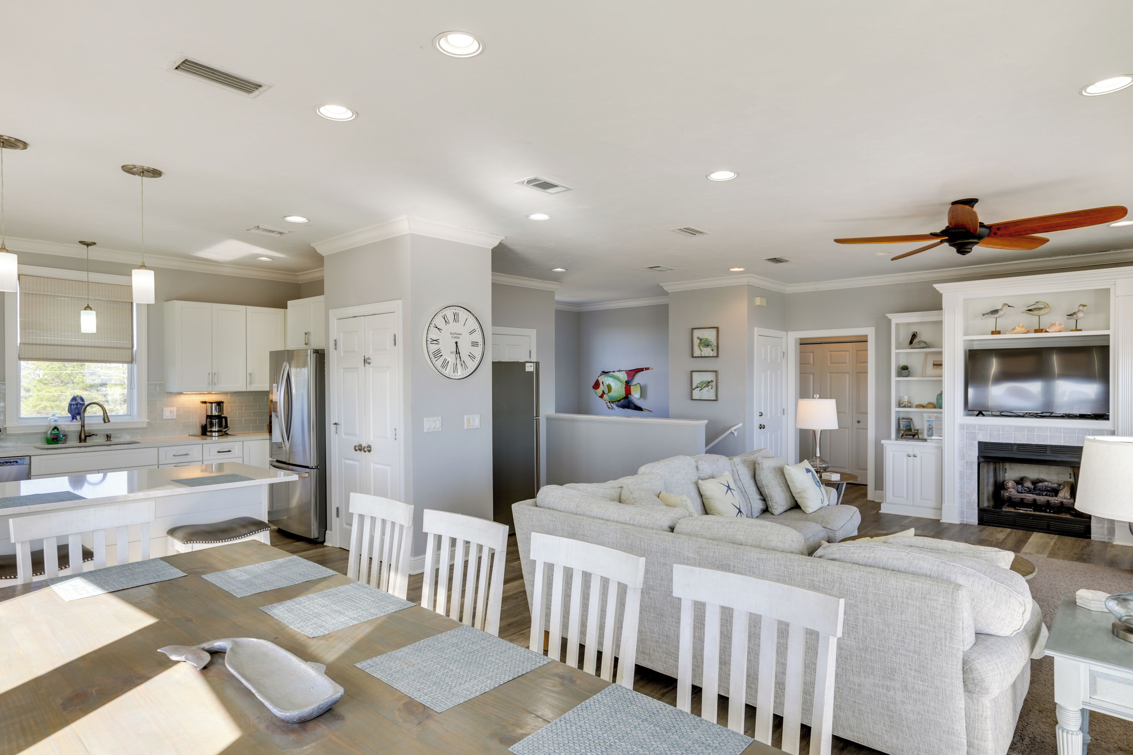 A modern kitchen with white cabinetry, a stainless steel refrigerator, and a dining area with a wooden table and white chairs.