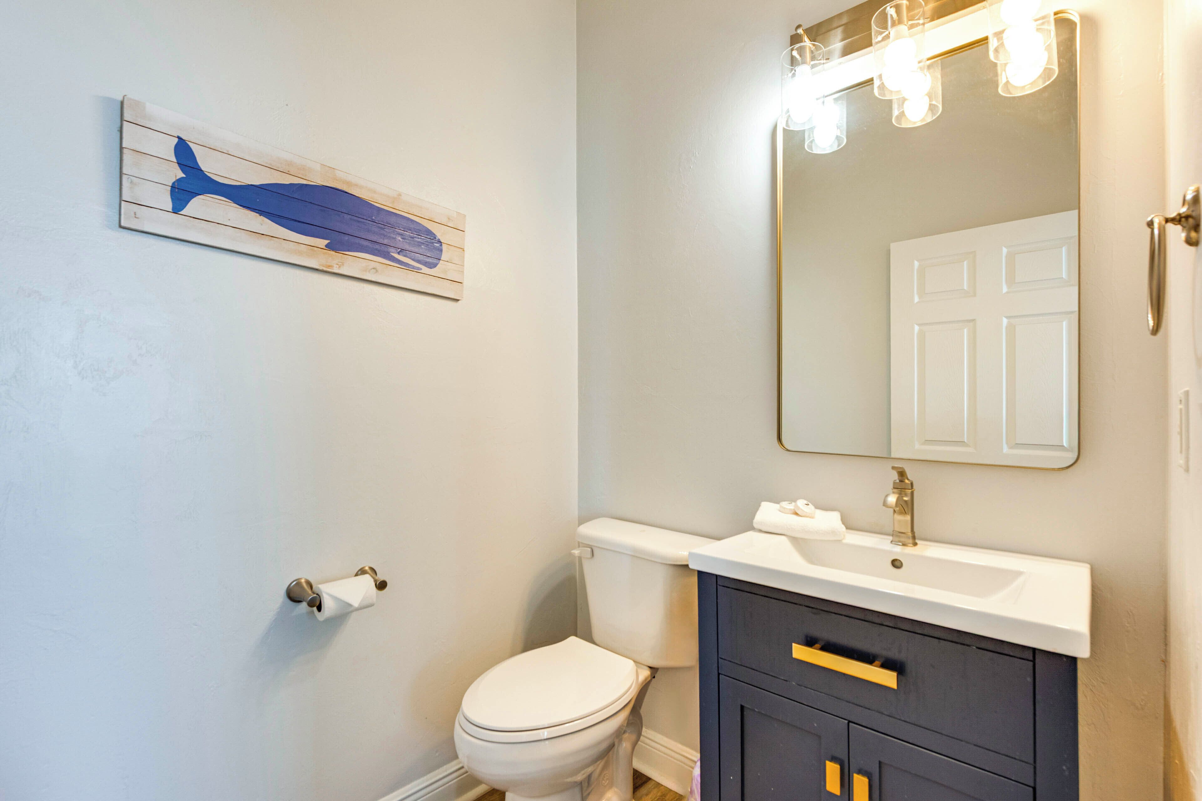 Une salle de bain avec des toilettes blanches, un meuble-lavabo foncé doté d’un miroir et un mur bleu clair.