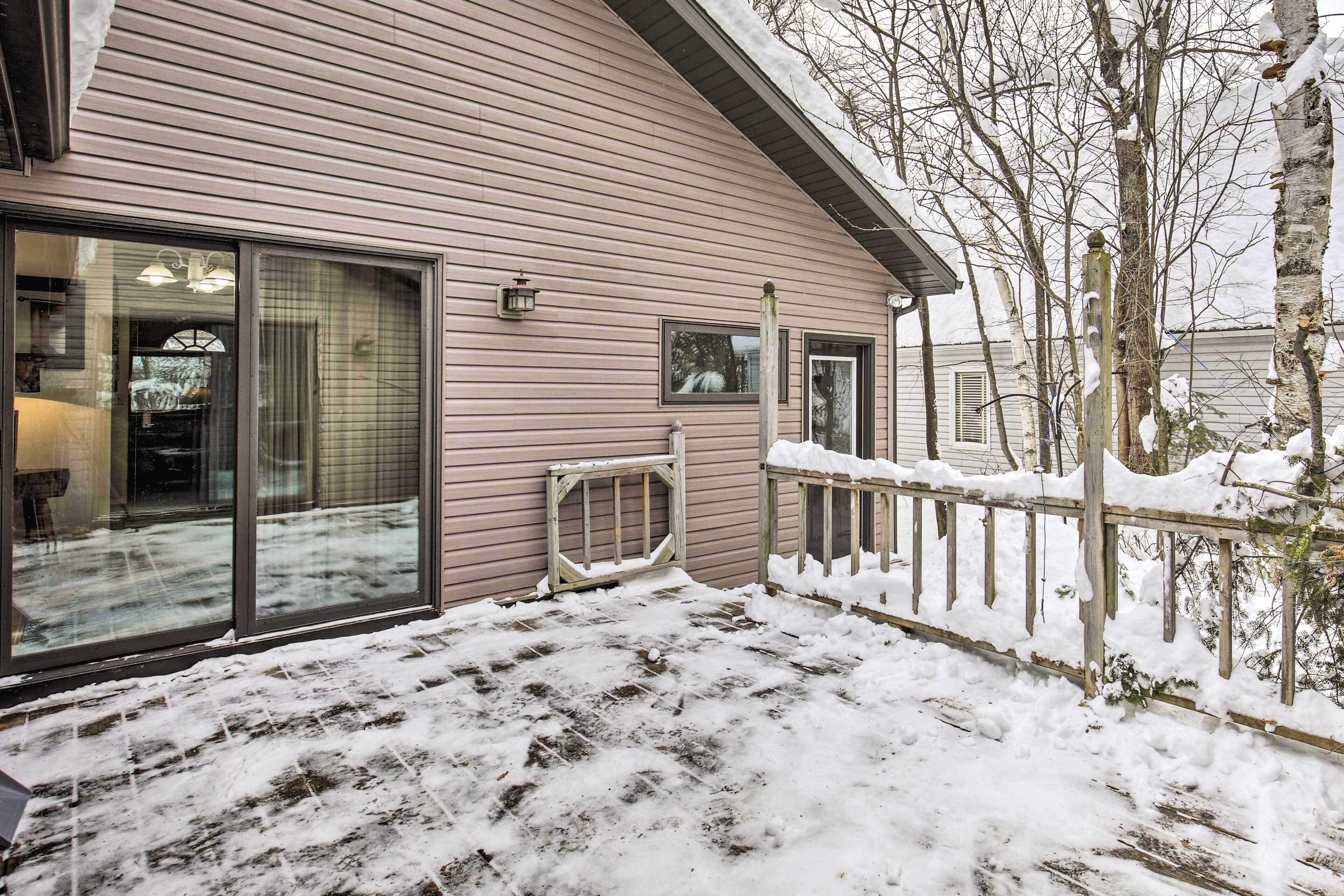 A house with large sliding glass doors, a wooden deck, and a snow-covered yard.