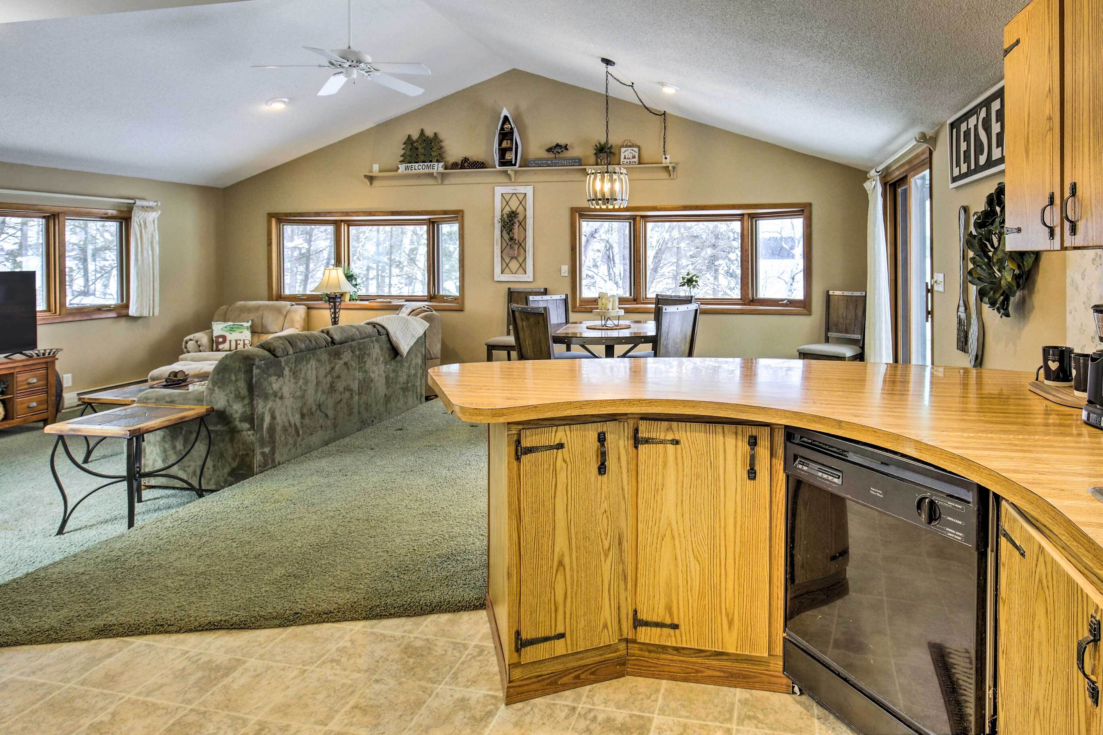 A kitchen with a wooden island, a dining area with a table and chairs, and a living room with a sofa and a television.
