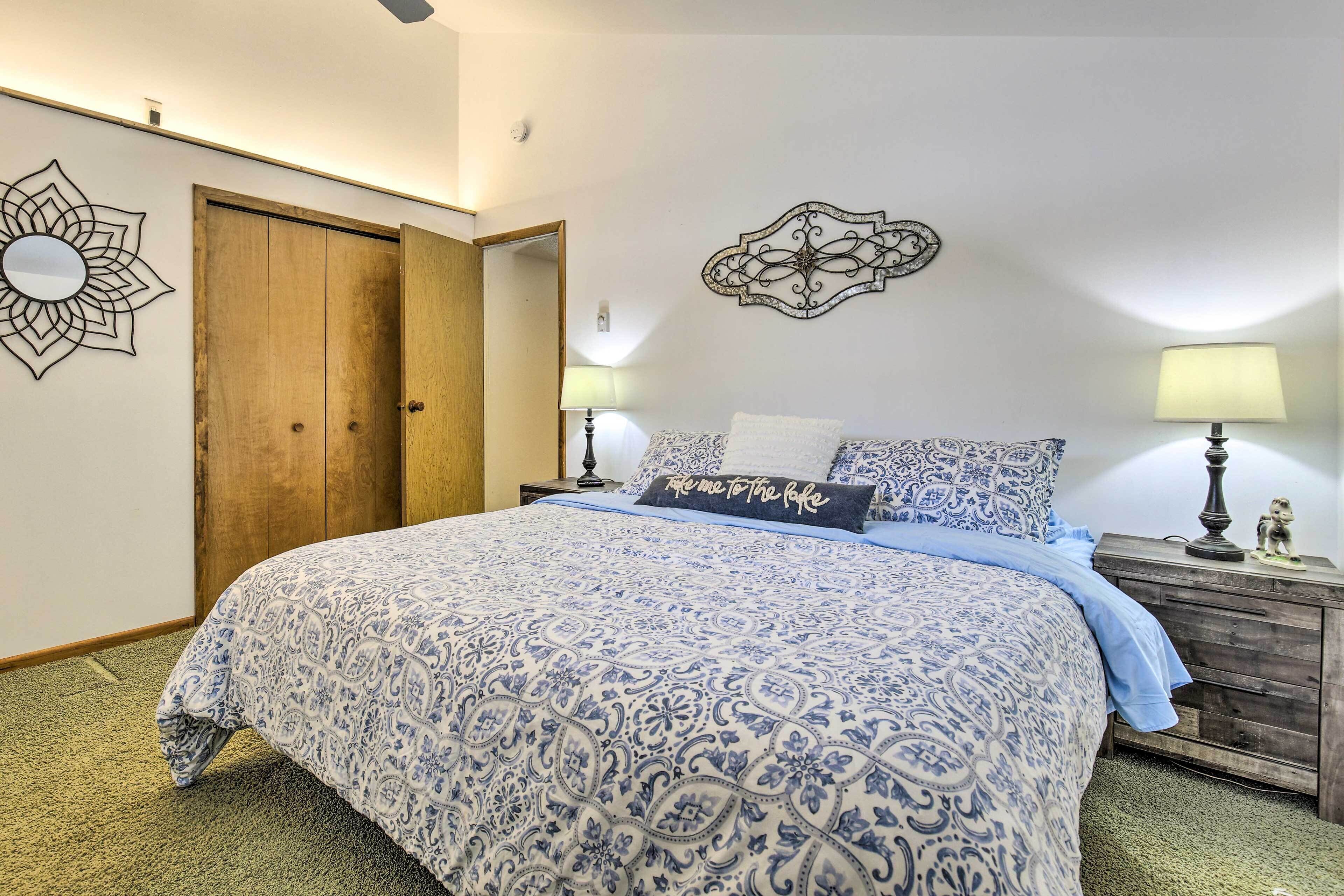 A bedroom with a large bed, two bedside tables with lamps, a wooden wardrobe, and decorative wall art.