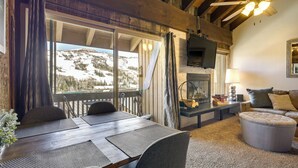 A cozy room with a wooden ceiling, a fireplace, a TV mounted on the wall, a dining table with chairs, and a view of a snowy mountain. - Townhome w/ Mtn View - Walk to Brian Head Lifts! (Brian Head)