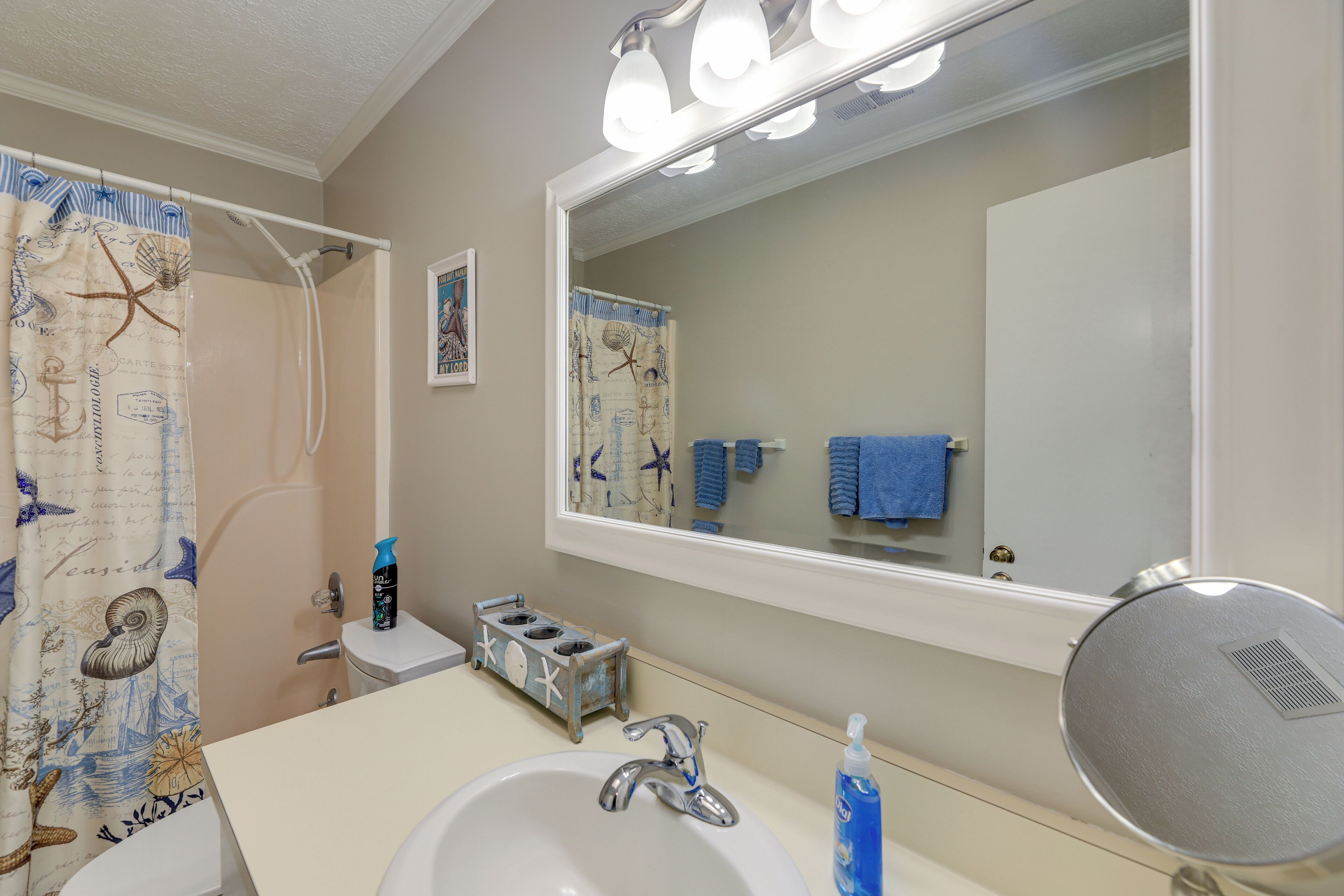 A bathroom with a sink, mirror, and shower curtain with nautical designs.
