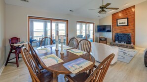A dining area with a wooden table, chairs, and a view of the outdoors through large windows.