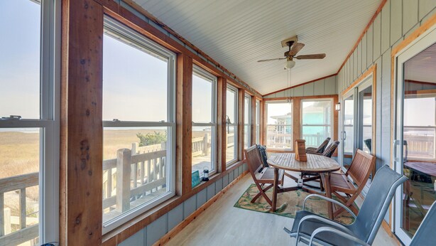 A covered outdoor area with a wooden table and chairs, large windows, and a view of the landscape.