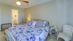 A bedroom with a bed, a ceiling fan, a nightstand, a chair, and a door leading to a bathroom.