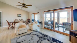 A spacious living room with a ceiling fan, a dining area with wooden chairs, a sofa, and a large sliding glass door leading to an outdoor patio.