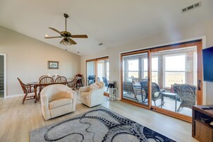 Amplia sala de estar con ventilador de techo, comedor con sillas de madera, sofá y un amplio ventanal corredero que da a un patio exterior.