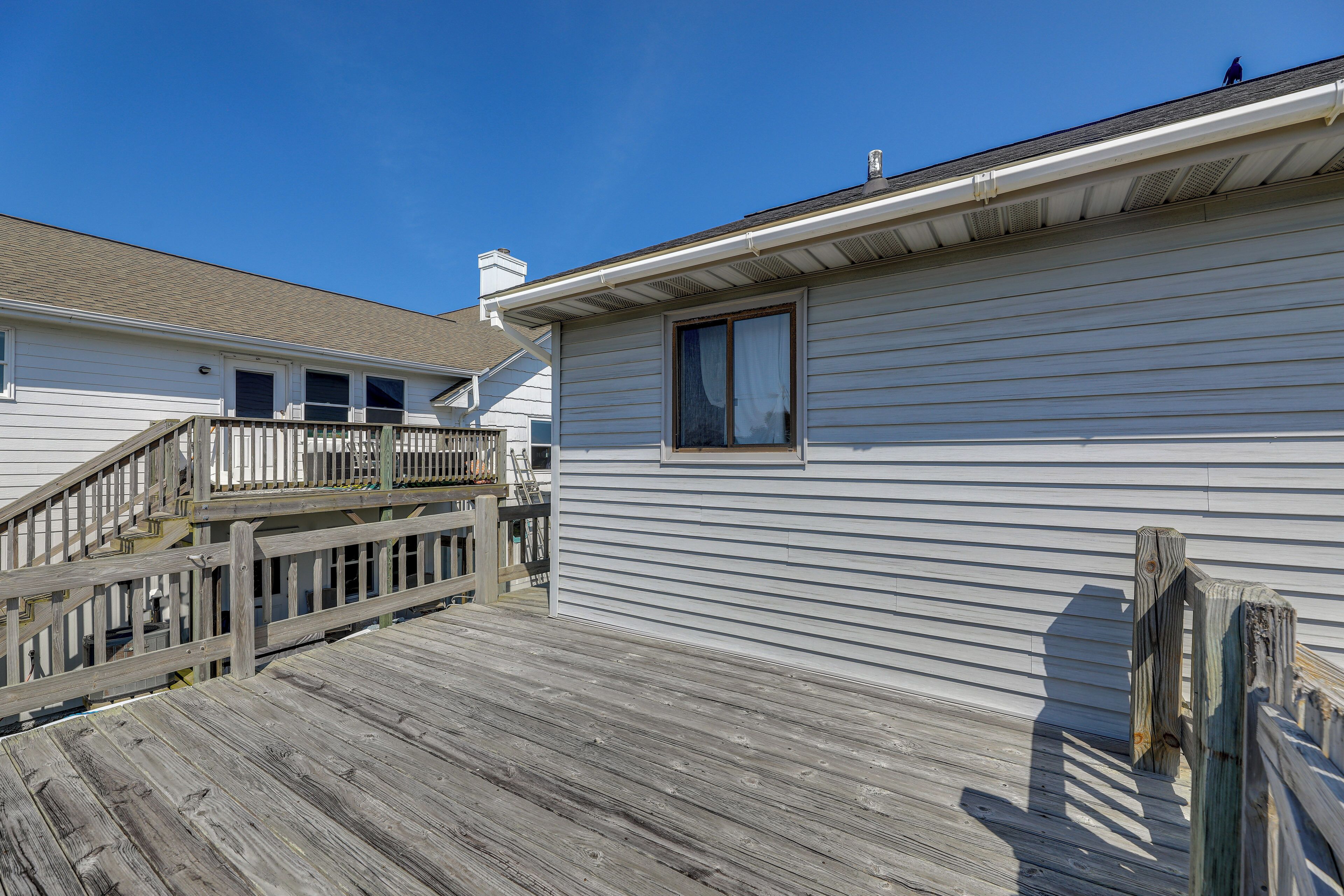 A wooden deck leading to a white house with a window and a chimney.