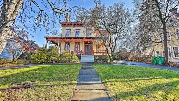 A two-story house with a front porch, a stone pathway leading to the entrance, and a green trash bin to the right. - Pet-friendly Apt in 1850's Victorian Mansion! (Poughkeepsie)