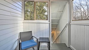 A covered porch with a chair and table, a staircase, and a view of trees through the windows. - Pet-friendly Apt in 1850's Victorian Mansion! (Poughkeepsie)