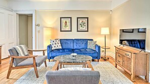 A living room with a blue sofa, a wooden coffee table, a grey armchair, and a wooden cabinet with a TV. - Pet-friendly Apt in 1850's Victorian Mansion! (Poughkeepsie)
