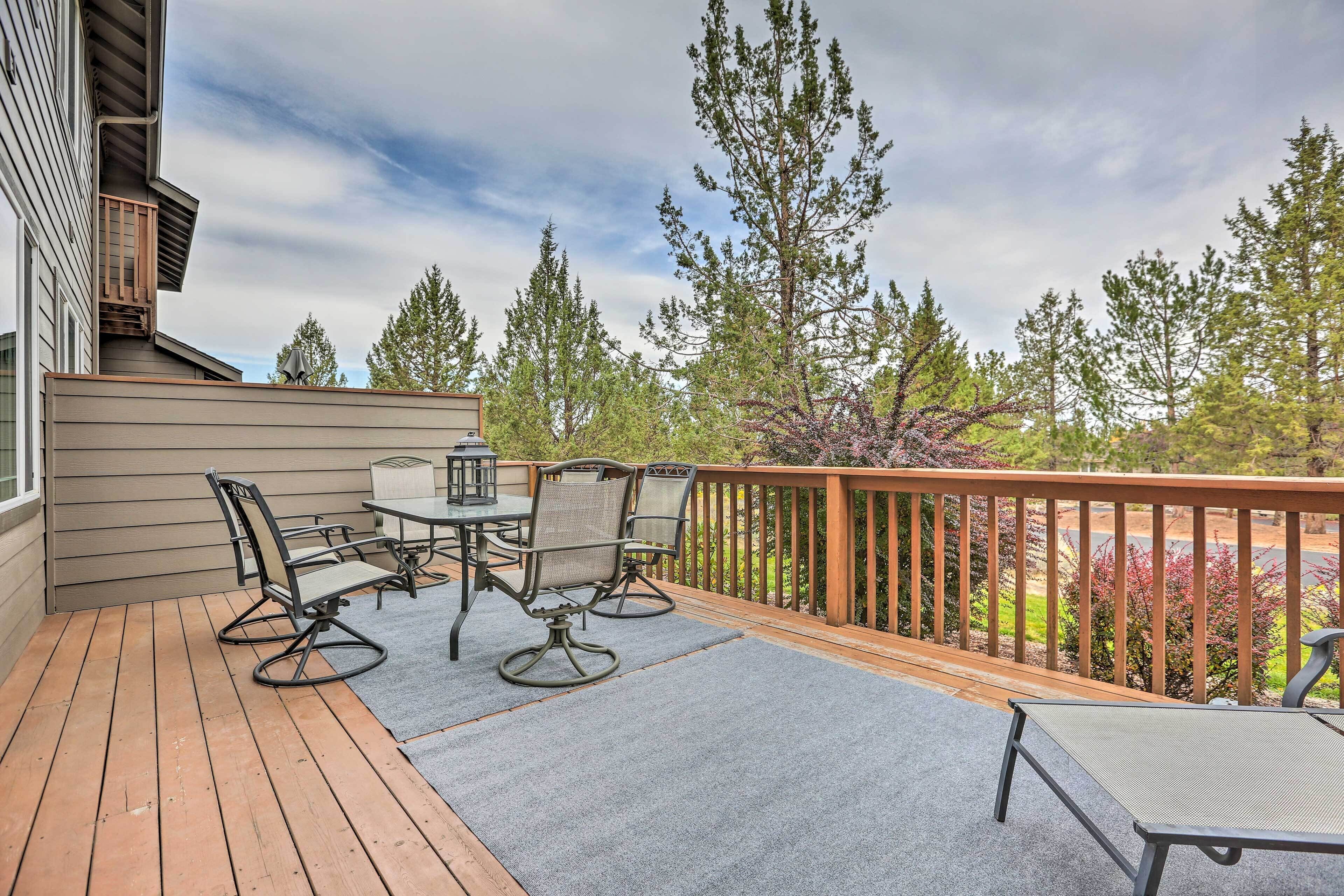 A deck with outdoor furniture, a railing, and a view of trees and a building.