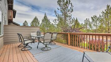 A deck with outdoor furniture, a railing, and a view of trees and a building.