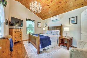 A bedroom with a wooden ceiling, a bed with a blue blanket, a wooden dresser, a television, and a window with a view. - Hot Tub, Fire Pit: Family-friendly Murphy Home (Murphy)