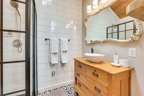 A bathroom with a glass shower enclosure, white tiled walls, a wooden vanity with a vessel sink, and a large mirror with an ornate frame. - Hot Tub, Fire Pit: Family-friendly Murphy Home (Murphy)