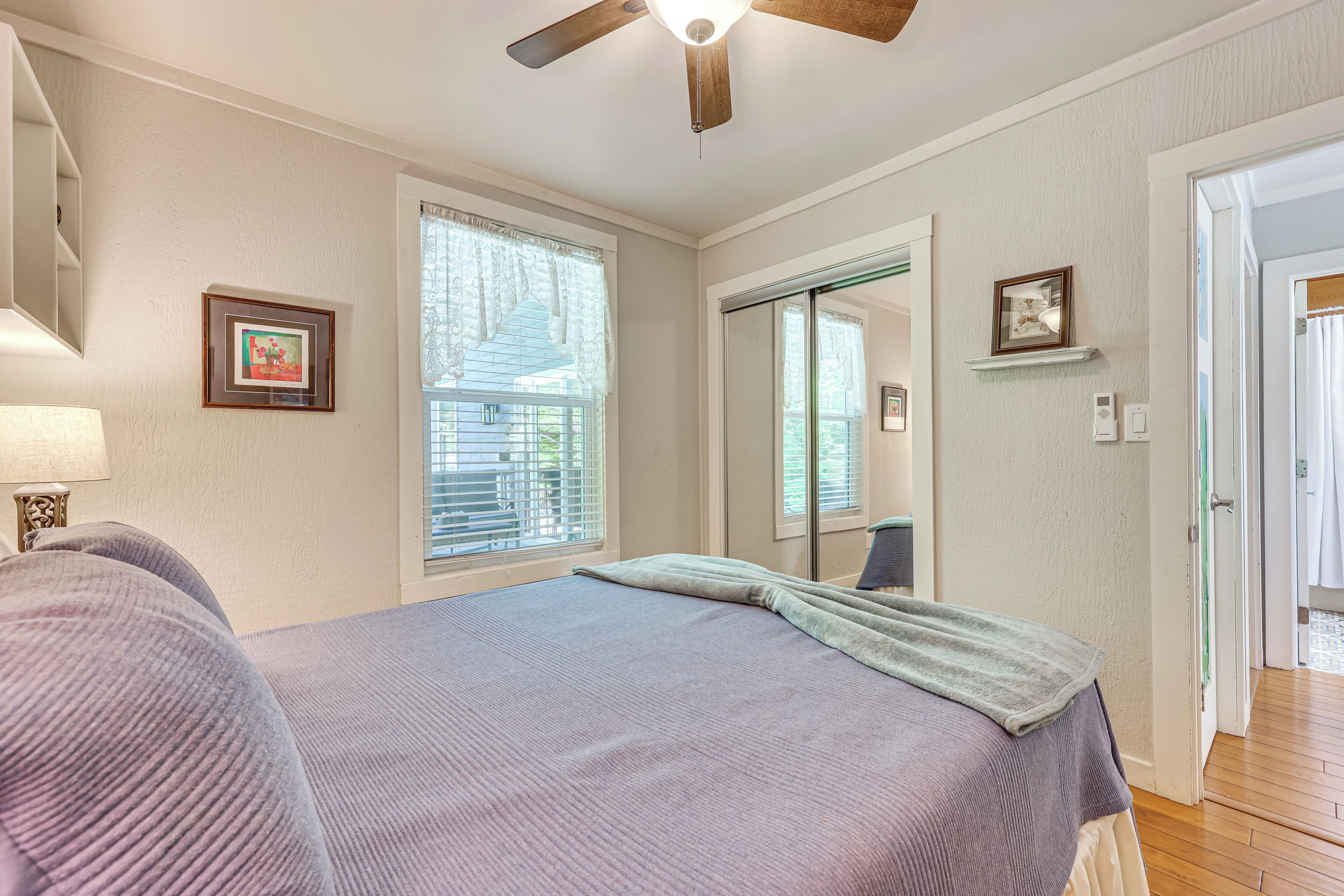 Une chambre à coucher comprenant un lit, un ventilateur de plafond, une fenêtre avec des stores, une porte et un miroir.