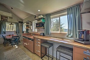 Une cuisine moderne dotée d’un îlot central, de tabourets de bar, d’un coin repas avec une table et des chaises, et de grandes fenêtres avec des rideaux.