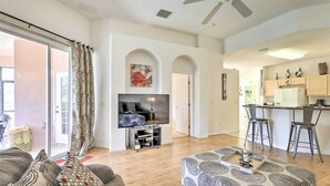 A living room with a sofa, ottoman, and TV stand. There is a kitchen area with bar stools and a refrigerator. - Family-friendly Escape w/ Smart TVs & Themed Rooms (Davenport)