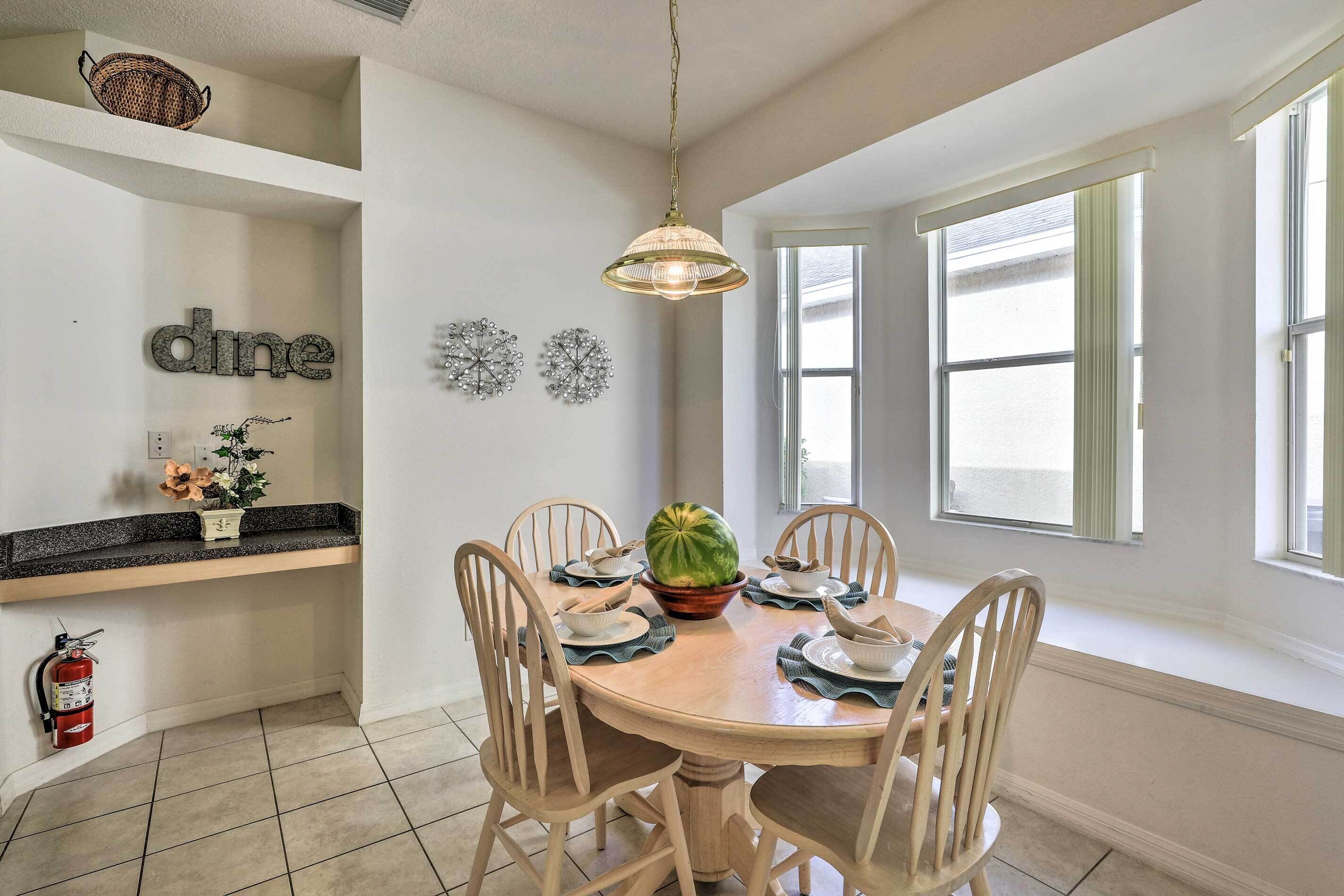 A dining area with a round table, six chairs, a hanging light fixture, a fire extinguisher, and decorative wall art.
