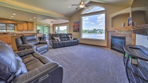 A spacious living room with leather sofas, a fireplace, and large windows offering a view of the outdoors. - Idyllic Idaho Falls Retreat w/ River Views! (Rigby)