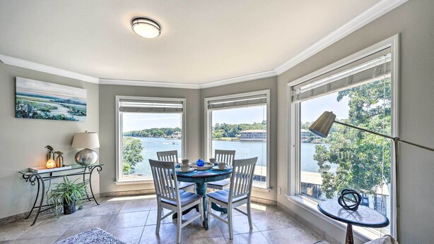 A dining area with a table and chairs, a lamp, a small table with a lamp, and a view of a body of water through large windows. - 'lakeview Blue Oasis' in Hot Springs: Lake Access (Hot Springs)