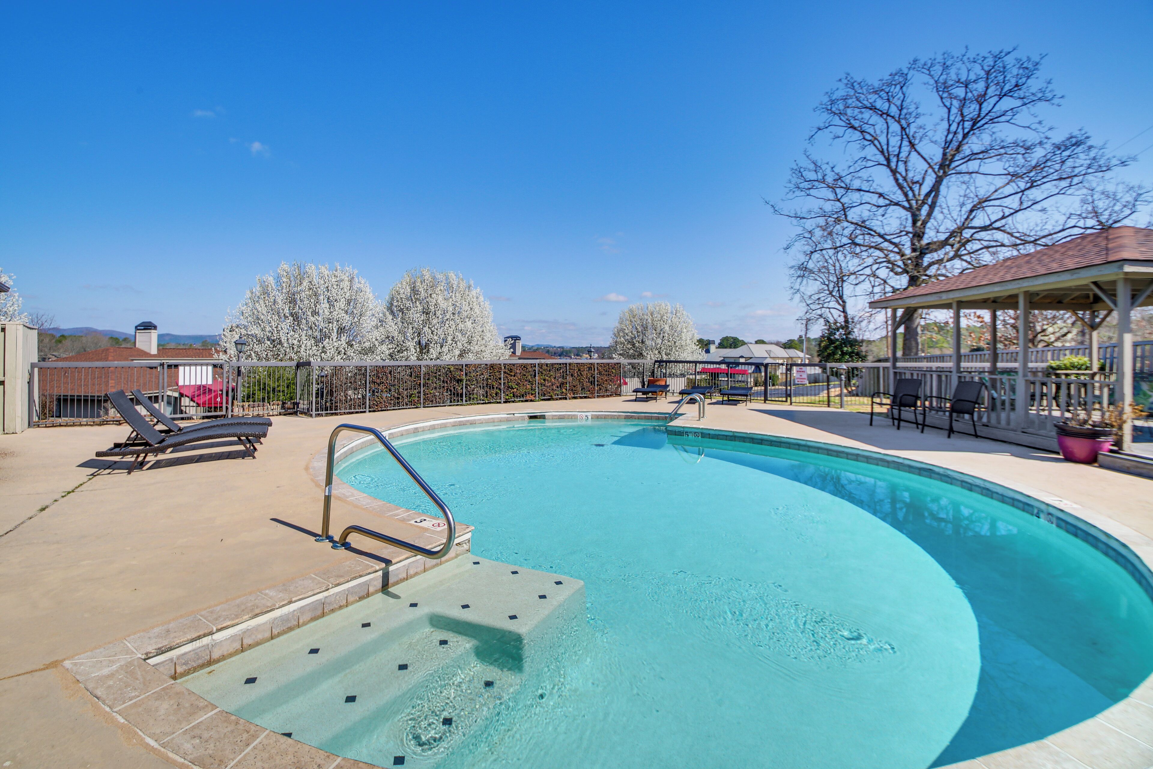 A swimming pool with a diving board, lounge chairs, and a covered seating area.