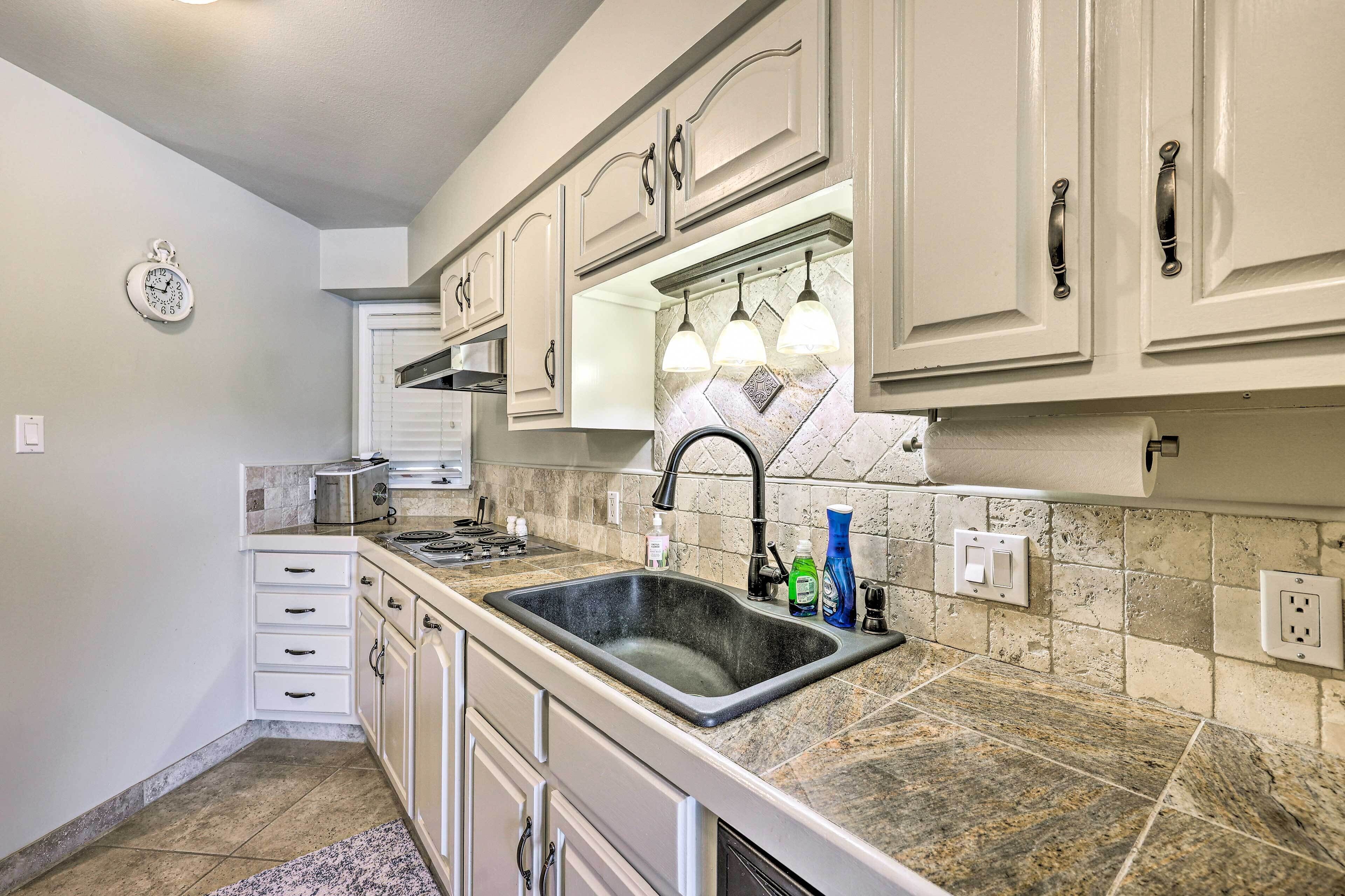 A kitchen with white cabinets, a granite countertop, a sink, and a clock on the wall.