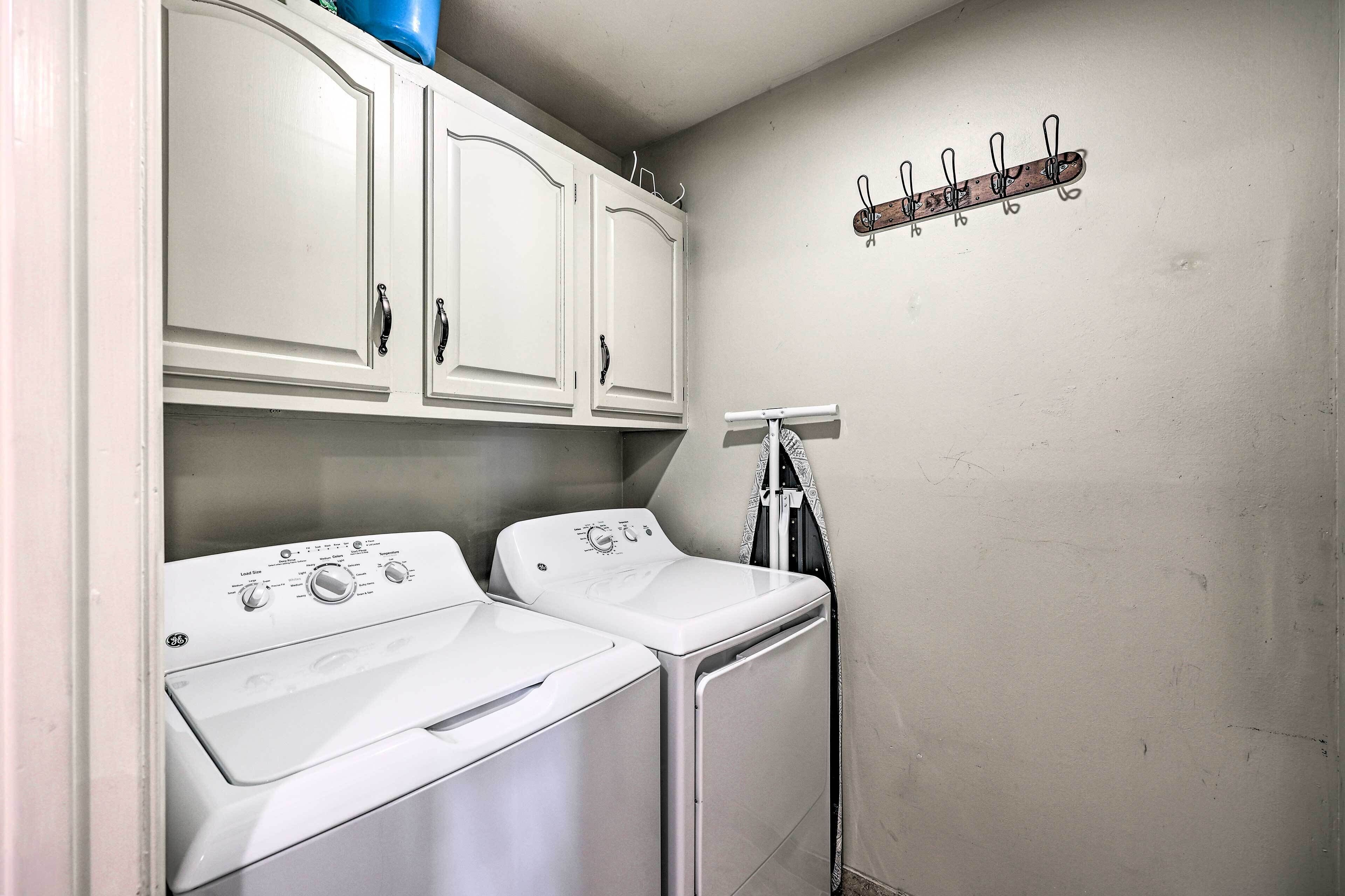 A laundry room with two front-loading washers and dryers, a metal rack with hooks, and a wall-mounted towel rack.