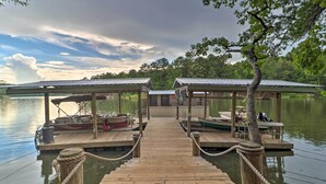 A wooden dock leading to covered boat docks with seating areas and a small building in the center. - Rustic-chic Riverfront Home w/ Dock, Deck & Canoes (Tallassee)